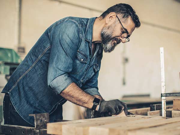 Mature male doing woodworking in a workshop while wearing glasses