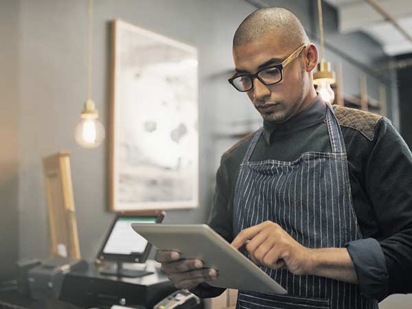 Young man in a small business, wearing glasses and working on a tablet device