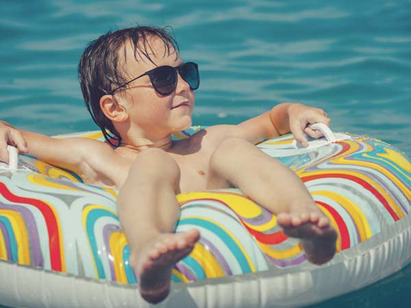 Kid sitting in a tube in the swimming pool while wearing sun glasses